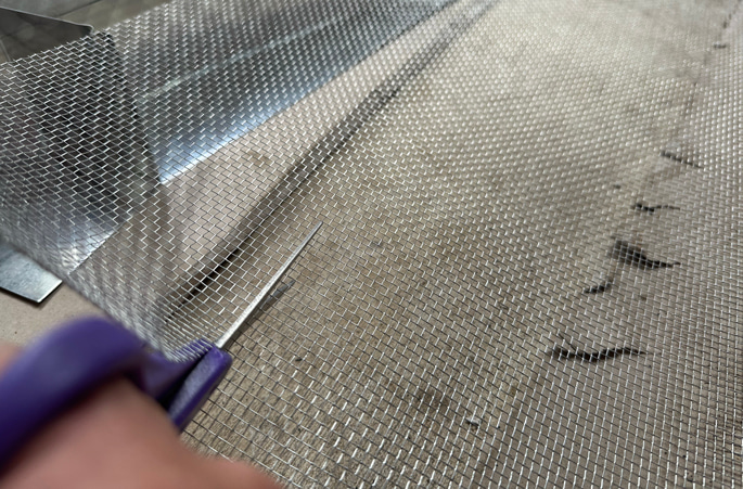 Cutting galvanized steel hardware cloth to size for installation.